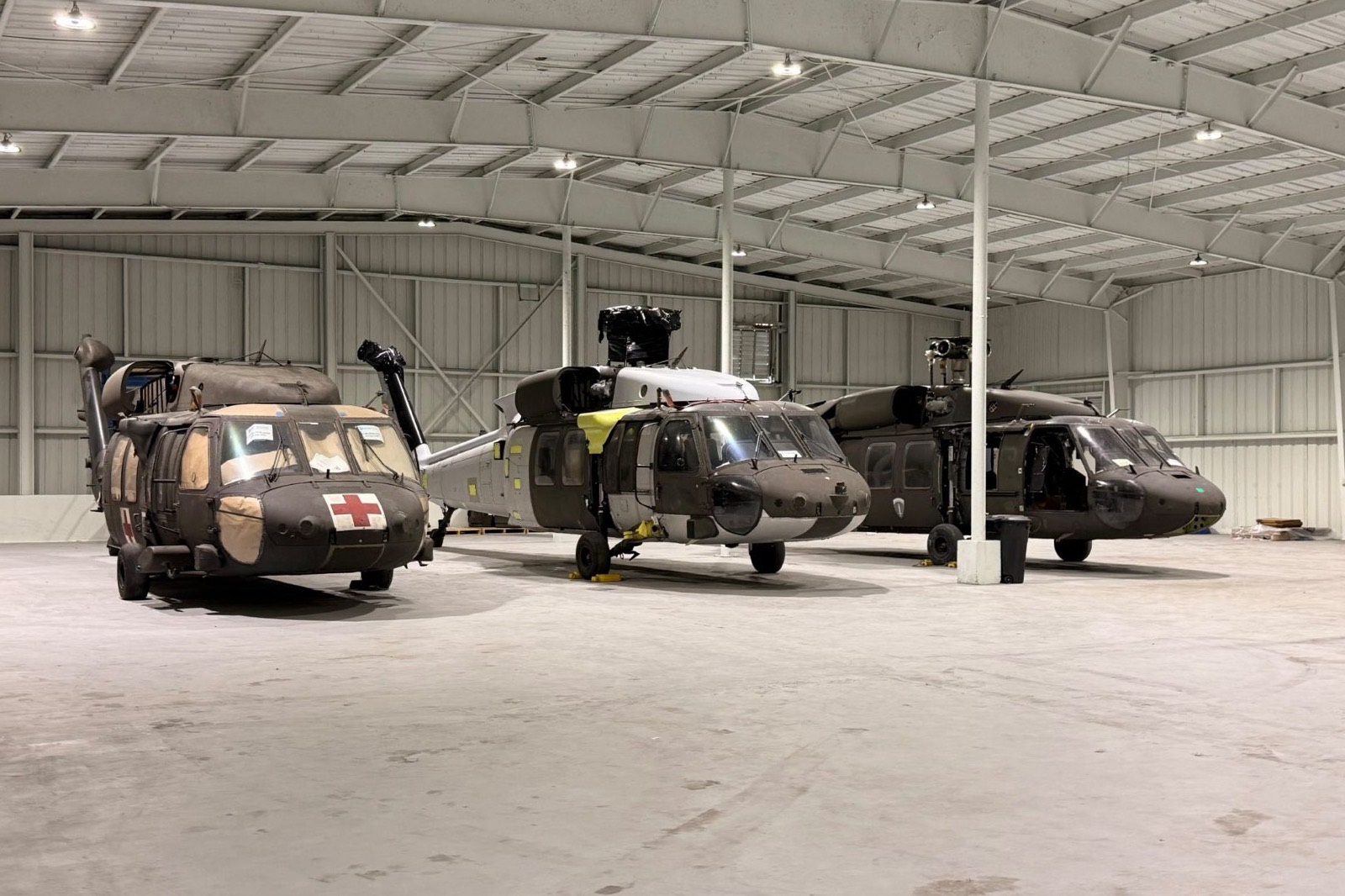 Three U.S. Army UH-60 Black Hawk helicopters staged in a hangar with rotor heads removed