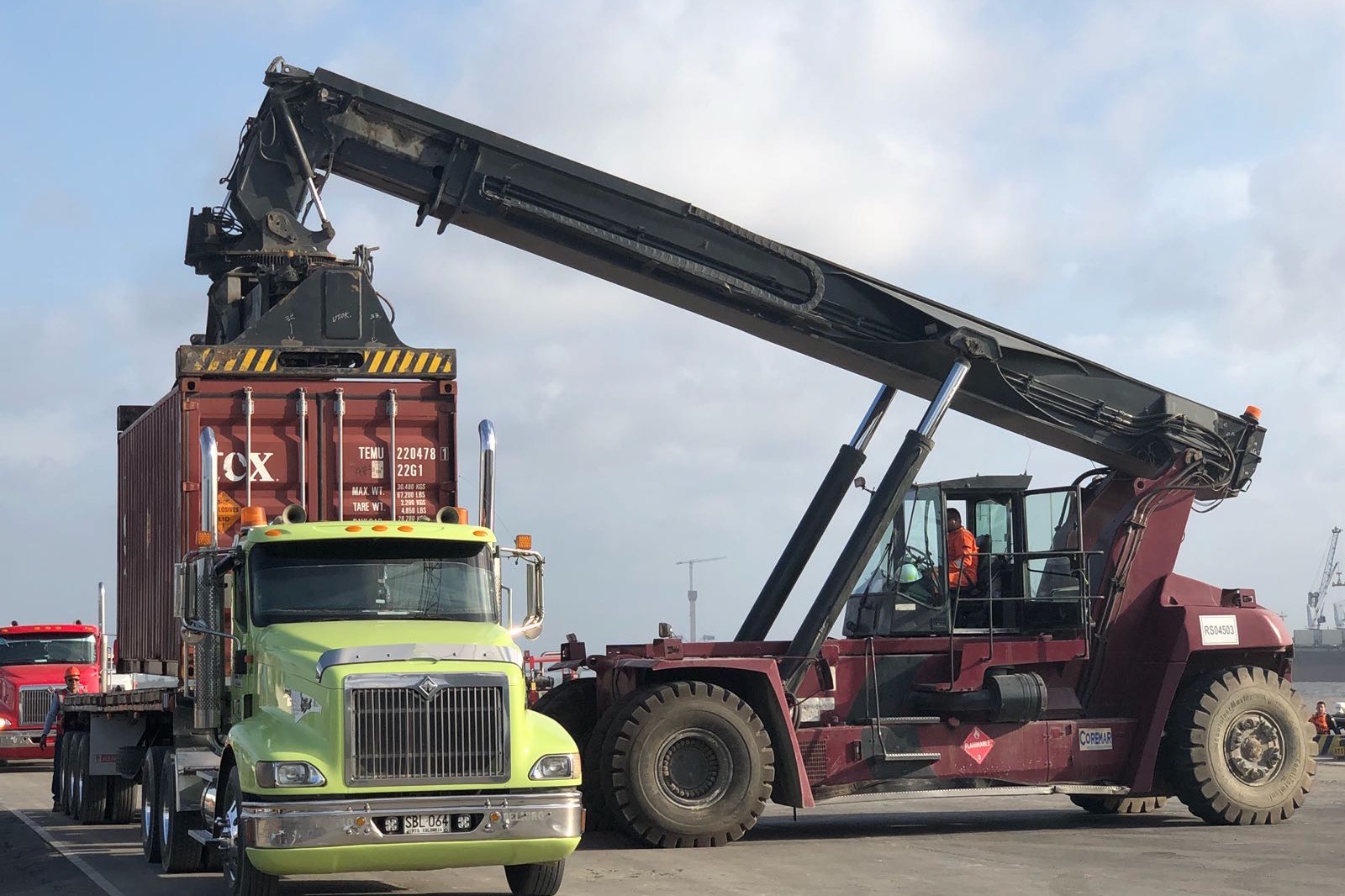 Reach stacker lifting a container placarded for Class 1 explosives onto a flatbed at a port